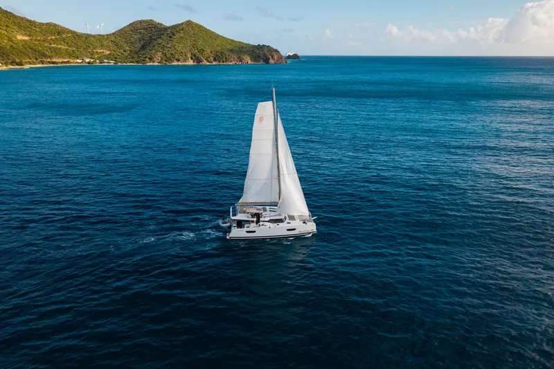 Ruckus Yacht Photos Pics 2021 Fountaine Pajot Elba 45 Catamaran sailing in open ocean near lush green hills.
