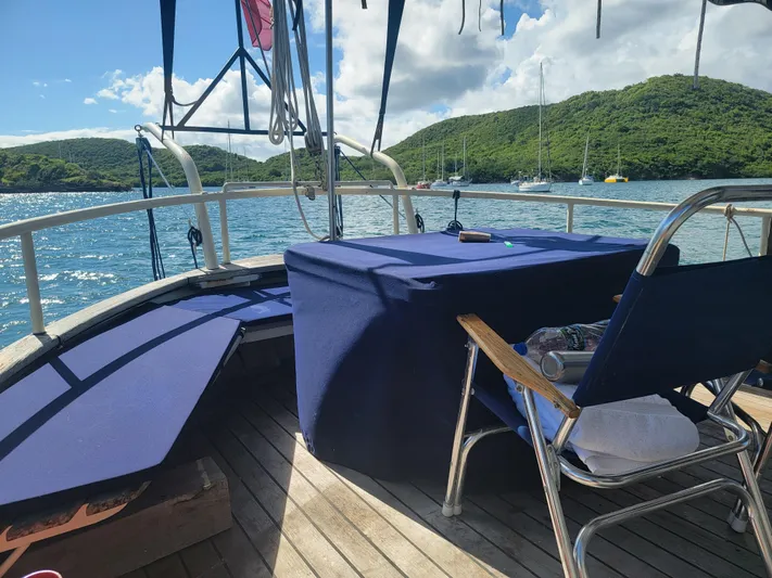 Maisie Rose Yacht Photos Pics Sailboat deck with blue seating, scenic view of lush green hills and calm waters.