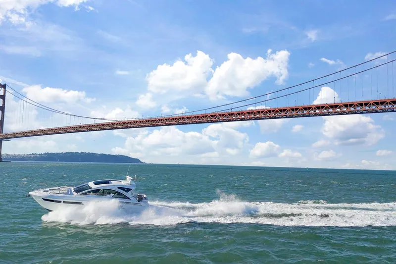 Simply Complicated Yacht Photos Pics 2019 Cruisers Yachts 54 Cantius cruising under a large bridge on a sunny day.