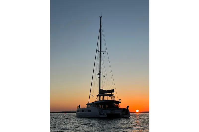  Yacht Photos Pics 2022 Lagoon 46 catamaran sailing at sunset on calm waters.