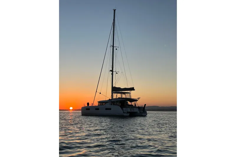  Yacht Photos Pics 2022 Lagoon 46 catamaran sailing at sunset on calm waters.