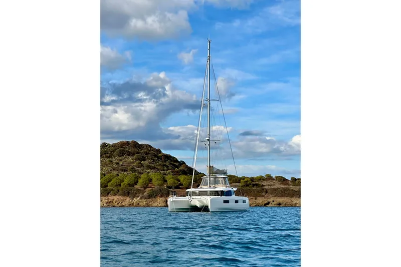  Yacht Photos Pics 2022 Lagoon 46 catamaran sailing near a scenic coastline under a blue sky.