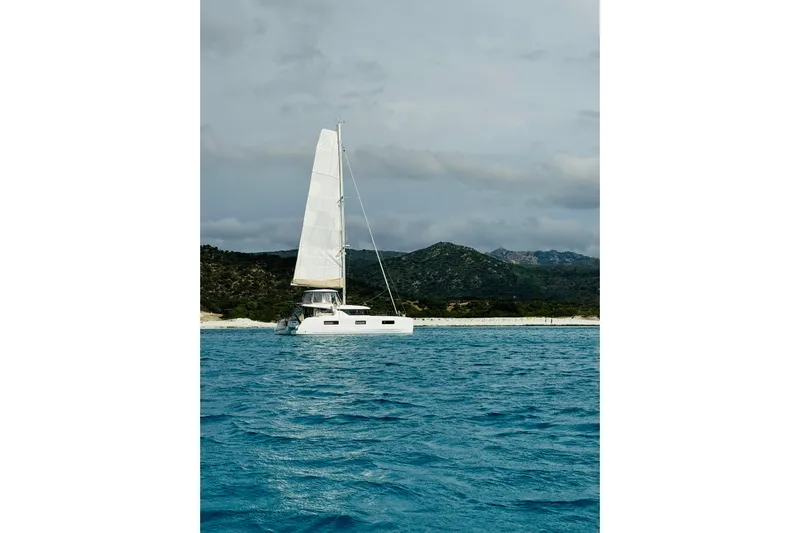  Yacht Photos Pics Sailing catamaran Lagoon 46 (2022) on blue water near a scenic coastline.
