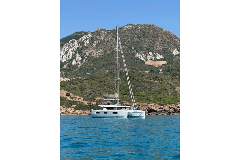  Yacht Photos Pics 2022 Lagoon 46 catamaran anchored near rocky coastline with lush greenery.
