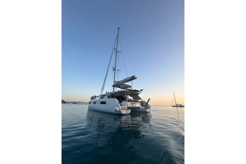  Yacht Photos Pics 2022 Lagoon 46 catamaran sailing at sunset on calm waters.