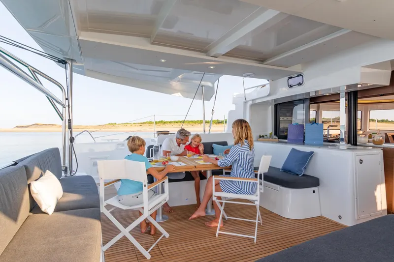  Yacht Photos Pics Family enjoying a meal on a 2022 Lagoon 46 catamaran, with scenic water views.