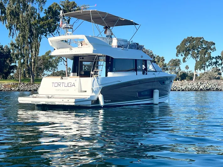 Tortuga Yacht Photos Pics 2017 Jeanneau Velasco 43F yacht on calm water, surrounded by trees and clear blue sky.