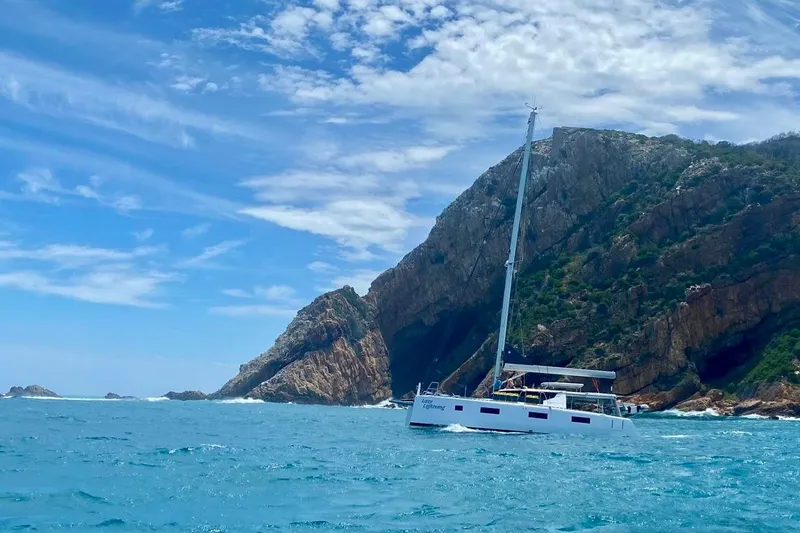 Lazy Lightning Yacht Photos Pics Sailboat Vision 444 (2021) cruising near rocky coastline under blue sky.