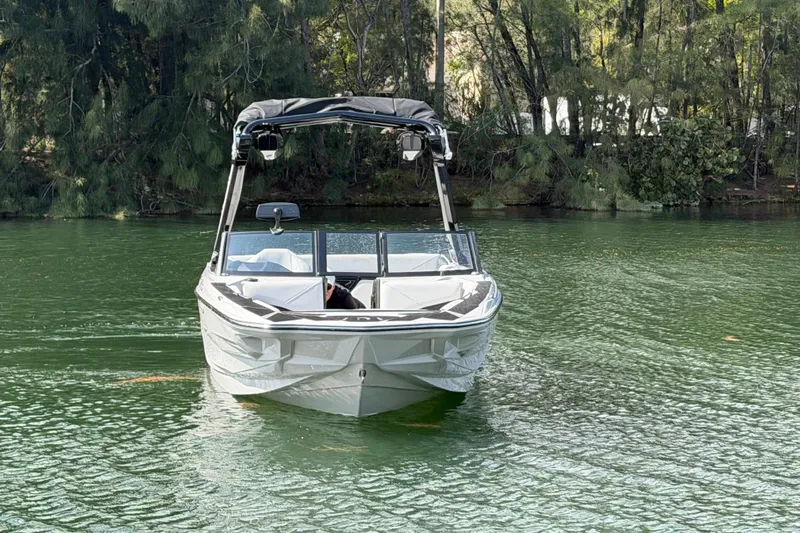  Yacht Photos Pics 2026 Centurion Nv233 boat on a serene lake with lush forest backdrop.
