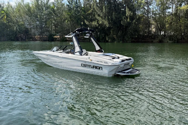  Yacht Photos Pics 2026 Centurion Nv233 boat on a serene lake with lush trees in the background.