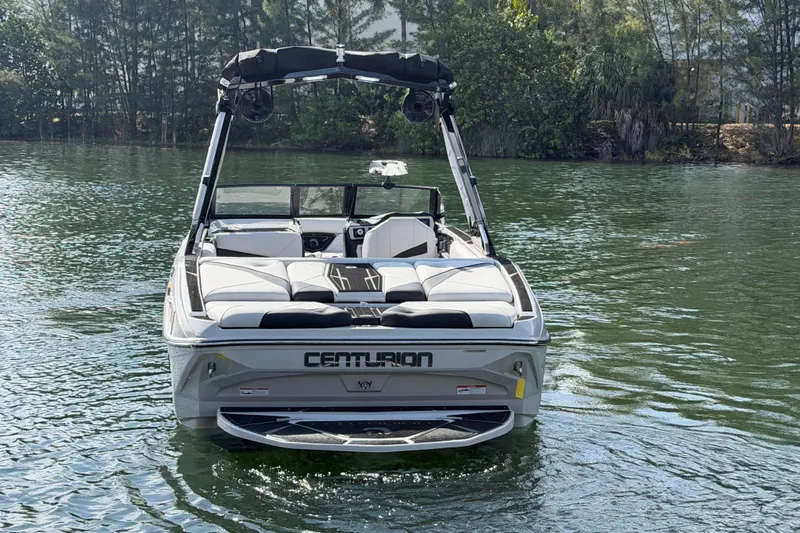 Yacht Photos Pics 2026 Centurion Nv233 boat on calm water, rear view with lush greenery background.