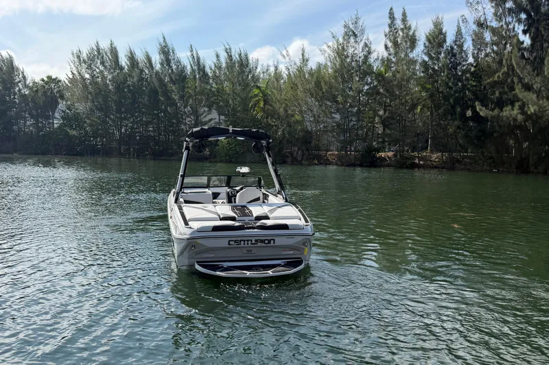  Yacht Photos Pics 2026 Centurion Nv233 boat on a serene lake with lush trees in the background.