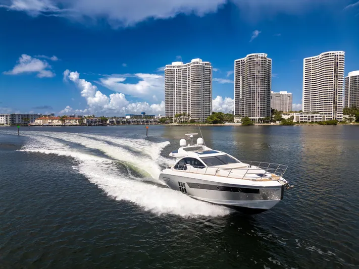 Ey IV Yacht Photos Pics 2016 Azimut 55S yacht cruising near modern high-rise buildings under a clear blue sky.