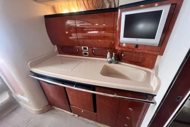 Wet Mess Yacht Photos Pics 2004 Sea Ray 360 Sundancer interior with kitchenette and TV, featuring wood cabinetry and sink.