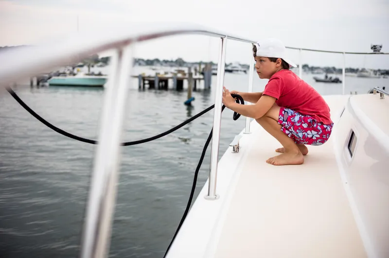 Dayglow Yacht Photos Pics Boy on MJM 53z boat holding rope, wearing red shirt and shorts, near marina.