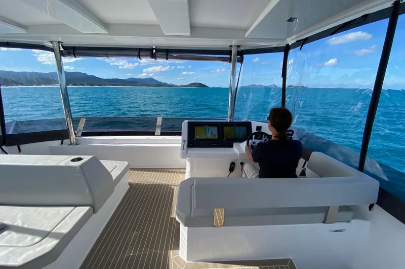  Yacht Photos Pics Person steering 2022 Leopard 46 Powercat yacht on open sea, clear skies, and scenic coastline.