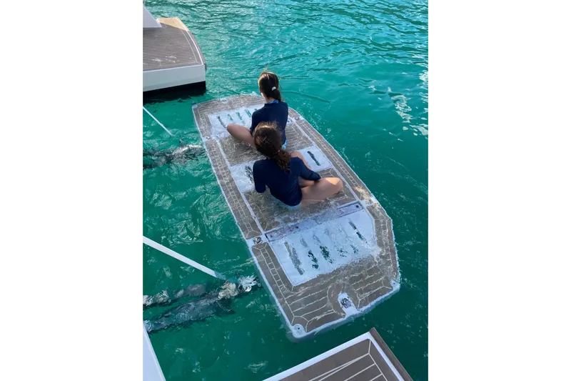  Yacht Photos Pics Two people sitting on a Leopard 46 Powercat swim platform, 2022 model, in clear blue water.