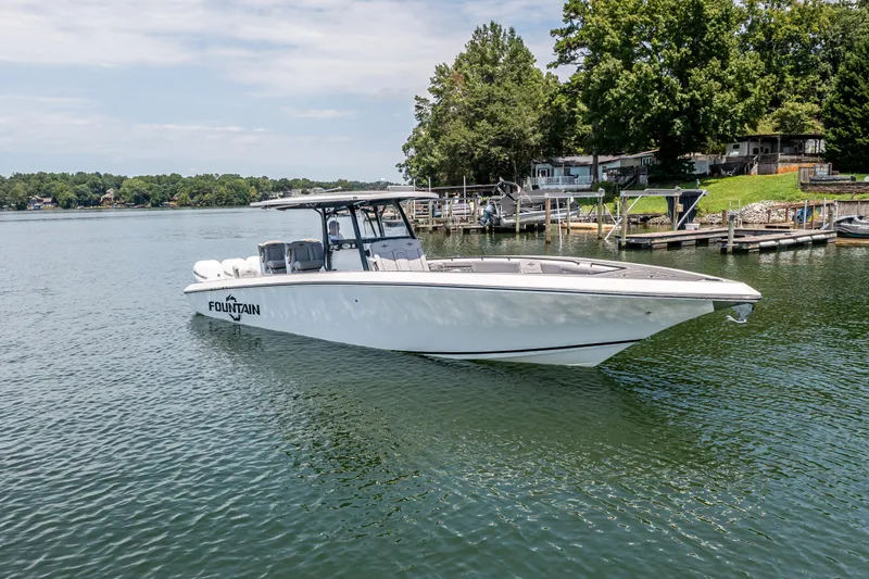 Yacht Photos Pics 2023 Fountain 38 SC boat on a serene lake near docks and trees.