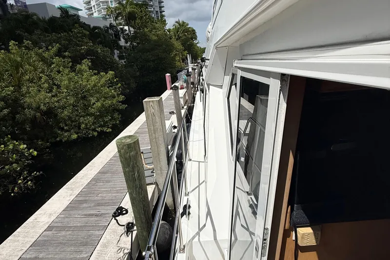 The Motley Crew Yacht Photos Pics 2003 Rival 5700 Navigator yacht docked beside lush greenery and modern buildings.