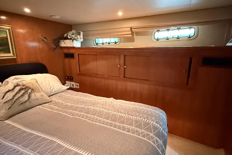 The Motley Crew Yacht Photos Pics Cozy bedroom interior of 2003 Rival 5700 Navigator yacht with wooden paneling and decorative pillows.