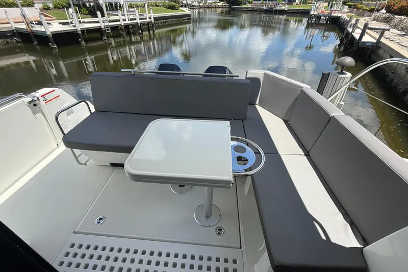  Yacht Photos Pics 2024 Beneteau Antares 11 boat interior with seating and table, docked by a calm waterway.