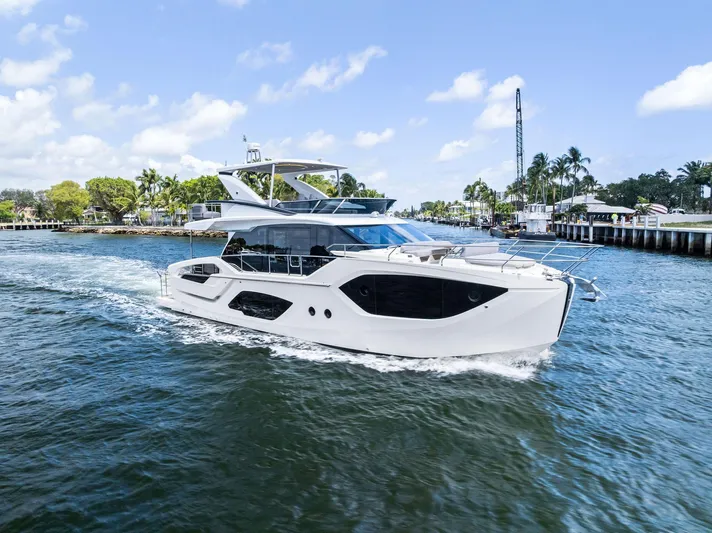 Lobster Tails Yacht Photos Pics 2023 Absolute 52 FLY yacht cruising on a sunny day, surrounded by water and palm trees.