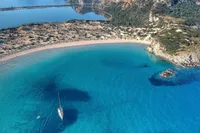 Aerial view of a Solaris 50 yacht in a serene, turquoise bay with sandy beach and rocky cliffs.