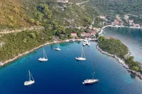 Aerial view of sailboats in a serene bay surrounded by lush greenery and coastal homes.