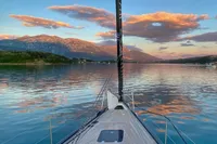 Sailing on a 2019 Solaris 50 yacht at sunset, with mountains and colorful clouds reflecting on water.