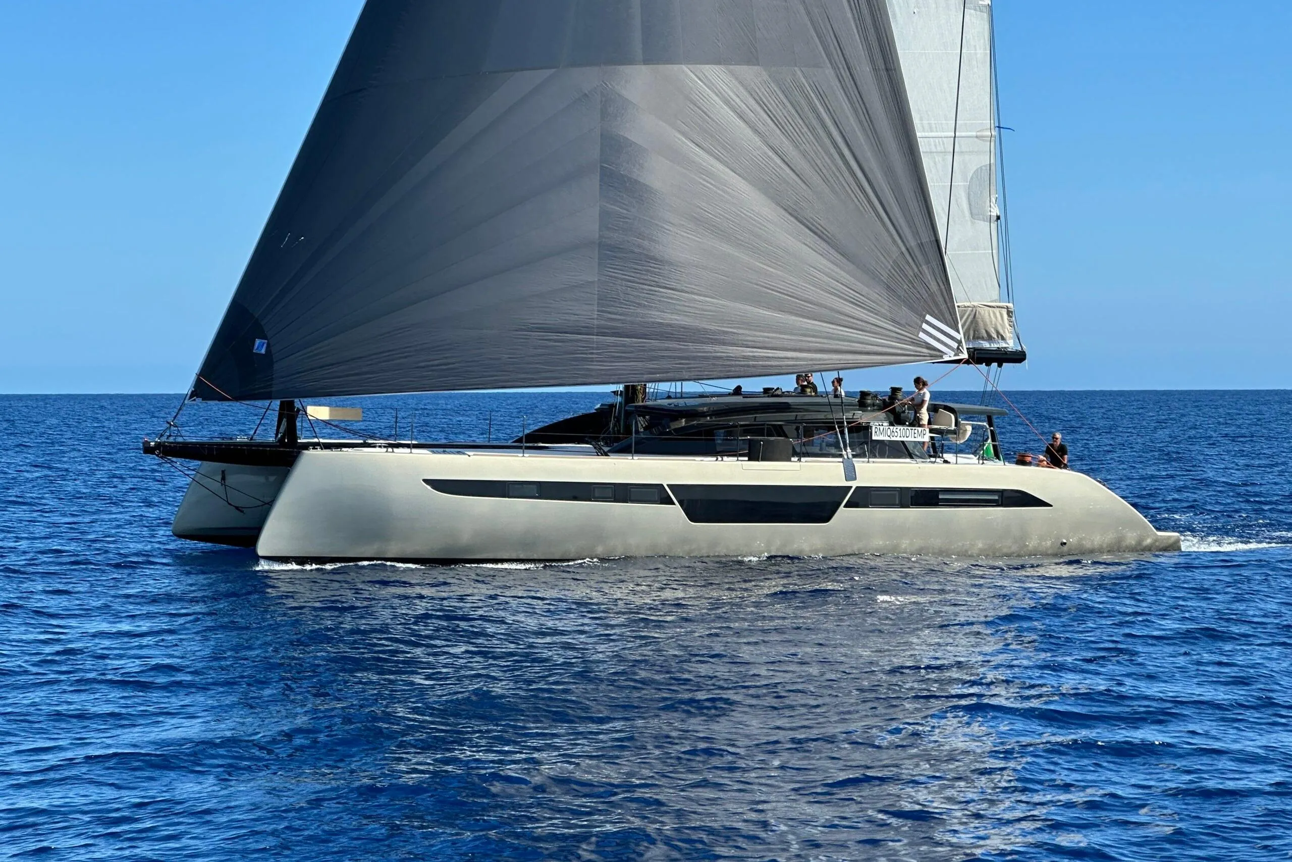 2026 Comar C-CAT 65 catamaran sailing on open sea with black sails.