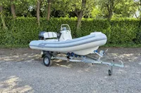 2022 AB Inflatables 11 ALX boat on trailer, parked on gravel with green foliage background.