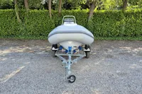 2022 AB Inflatables 11 ALX boat on trailer, parked on gravel with green hedge background.