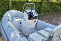 2022 AB Inflatables 11 ALX boat with steering console, parked on gravel near greenery.