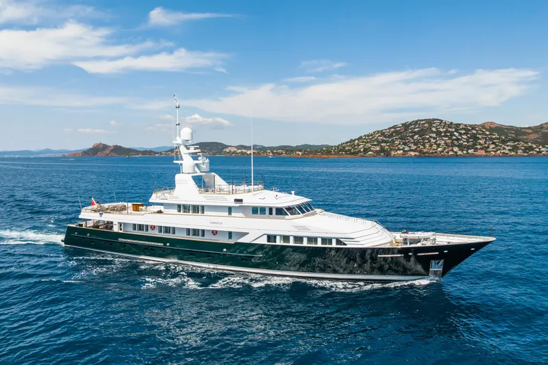 Emerald Yacht Photos Pics Luxurious 1990 Feadship yacht cruising in clear blue waters near scenic coastline.
