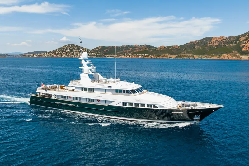 Emerald Yacht Photos Pics Luxurious 1990 Feadship yacht cruising in clear blue waters near scenic coastline.