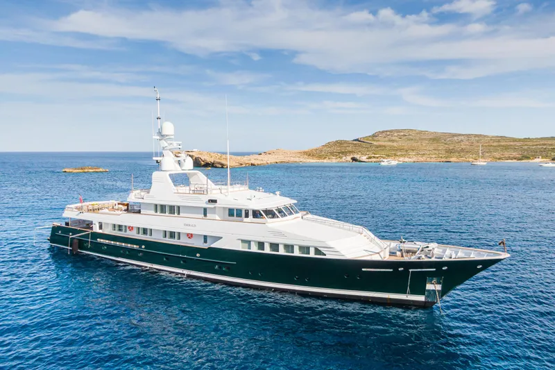 Emerald Yacht Photos Pics Luxurious 1990 Feadship yacht cruising in clear blue waters near a scenic coastline.