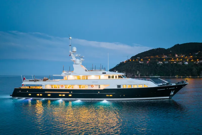 Emerald Yacht Photos Pics Luxurious 1990 Feadship yacht illuminated at dusk on serene waters.