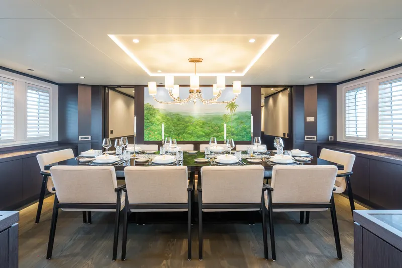 Emerald Yacht Photos Pics Luxurious dining room on 1990 Feadship yacht, elegant table setting, modern chandelier, scenic artwork.