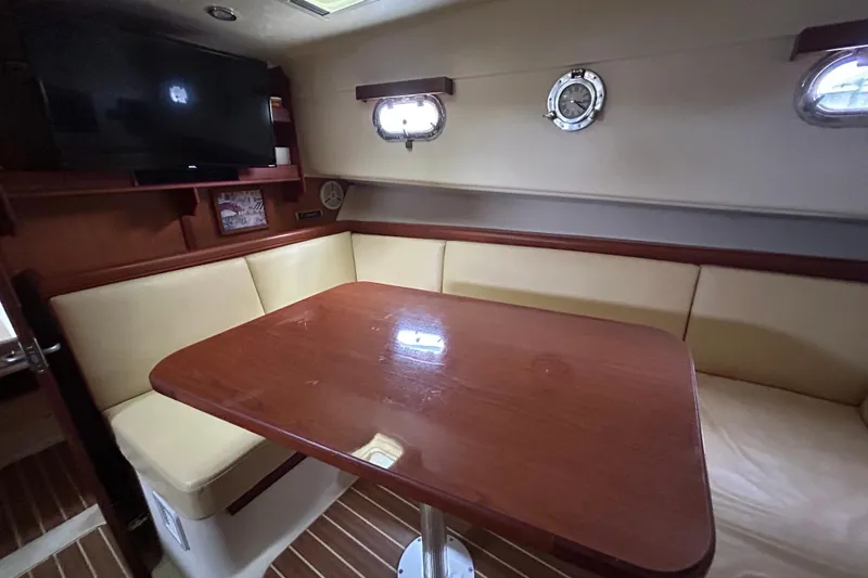 Eagle Yacht Photos Pics 2008 Mainship Pilot 34 interior with wooden table, beige seating, and mounted TV.