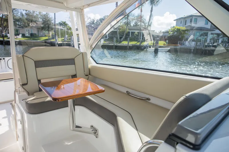 Joysea Yacht Photos Pics 2019 Pursuit DC 325 Dual Console interior with seating and wooden table, overlooking waterfront homes.
