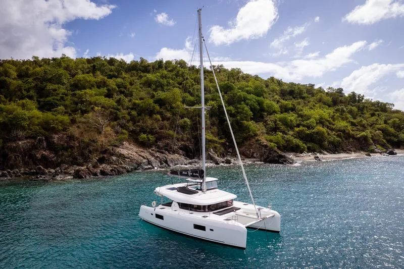 Tide Together Yacht Photos Pics 2023 Lagoon 42 catamaran sailing near lush green island coastline.