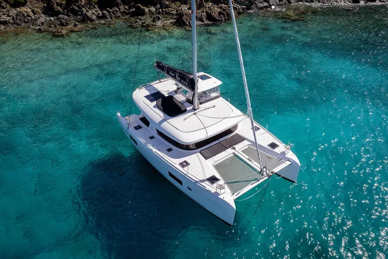 Tide Together Yacht Photos Pics 2023 Lagoon 42 catamaran sailing in clear turquoise waters near rocky shore.