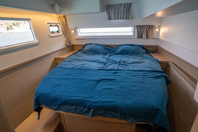 Tide Together Yacht Photos Pics 2023 Lagoon 42 yacht cabin with blue bedding and wooden interior design.