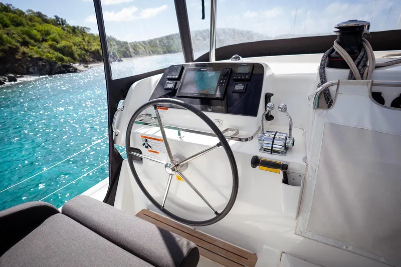 Tide Together Yacht Photos Pics Cockpit of 2023 Lagoon 42 catamaran with steering wheel and navigation controls, overlooking blue waters.