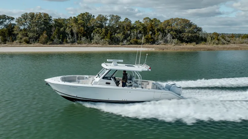 Mindy's Tyde III Yacht Photos Pics 2022 Pursuit S 328 boat cruising on a serene lake with a forested shoreline.