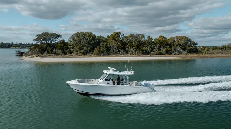 Mindy's Tyde III Yacht Photos Pics 2022 Pursuit S 328 boat cruising on a serene lake with a forested shoreline.