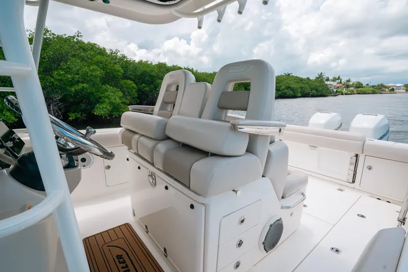 Rock N’ Doc Yacht Photos Pics 2019 Boston Whaler 330 Outrage boat interior with plush seating and steering wheel, near lush greenery.