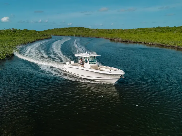 Rock N’ Doc Yacht Photos Pics 2019 Boston Whaler 330 Outrage cruising on a scenic waterway under a clear blue sky.