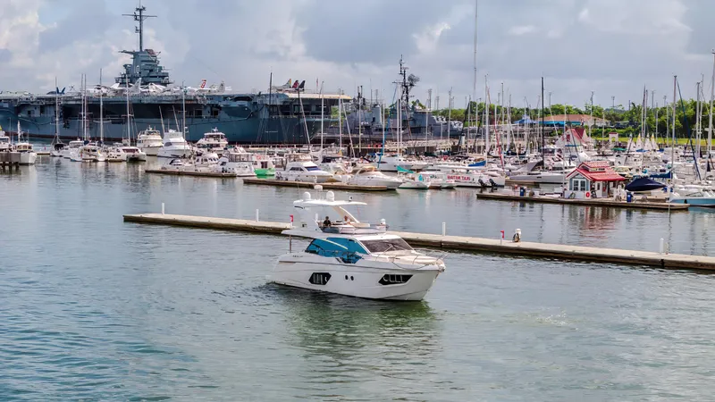 Tara Yacht Photos Pics Luxurious 2017 Absolute 50 Fly yacht in a bustling marina with naval ship backdrop.