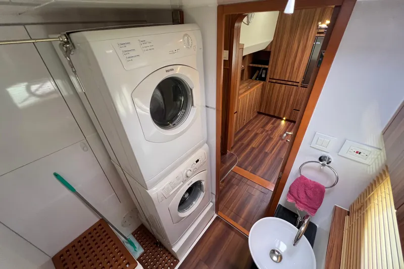 Tonga Time Yacht Photos Pics Laundry area with stacked washer-dryer in 2019 Aquila 44 yacht, featuring wooden flooring and compact sink.